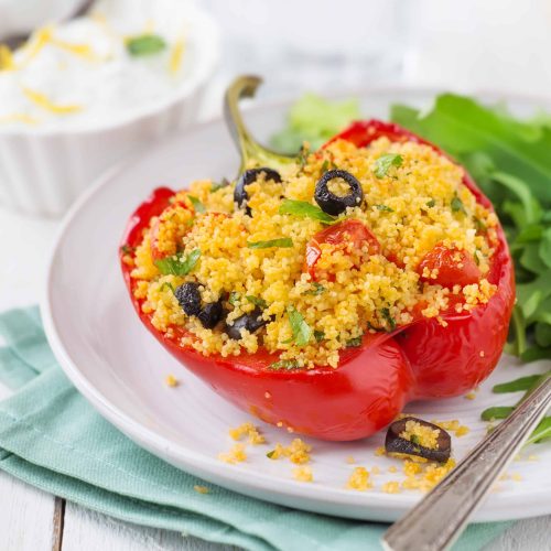 Vegetarian couscous stuffed pepper with rocket salad and yoghurt condiment on white wood background